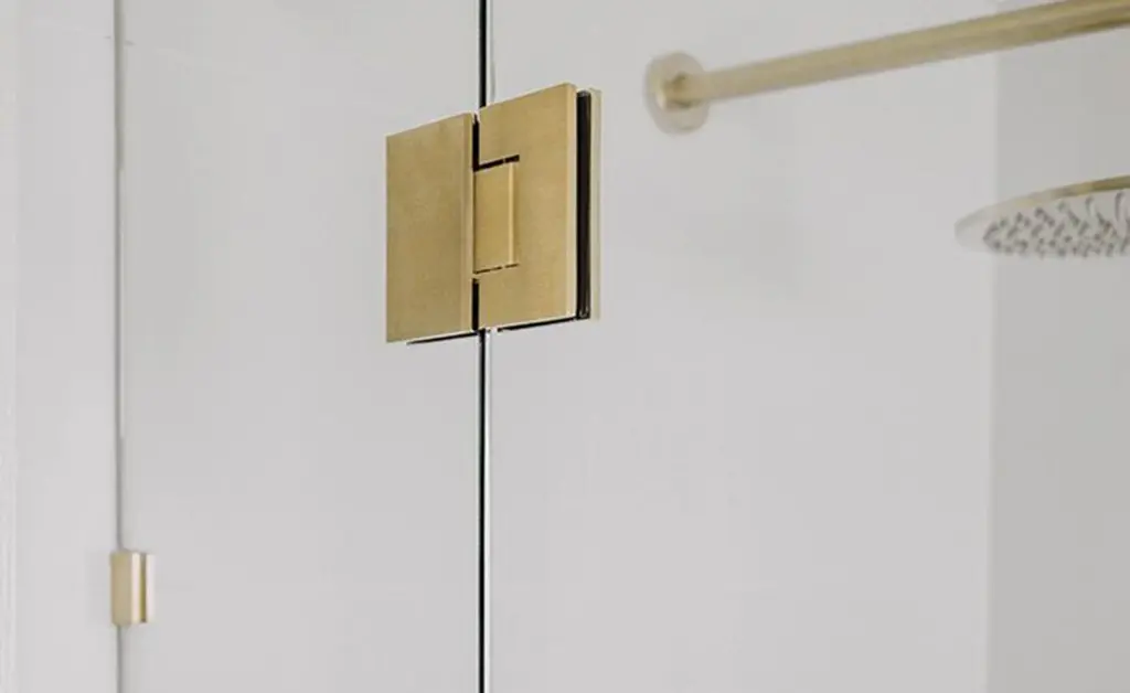 Brushed brass glass-to-glass shower hinge close-up showing metal finish and frameless installation