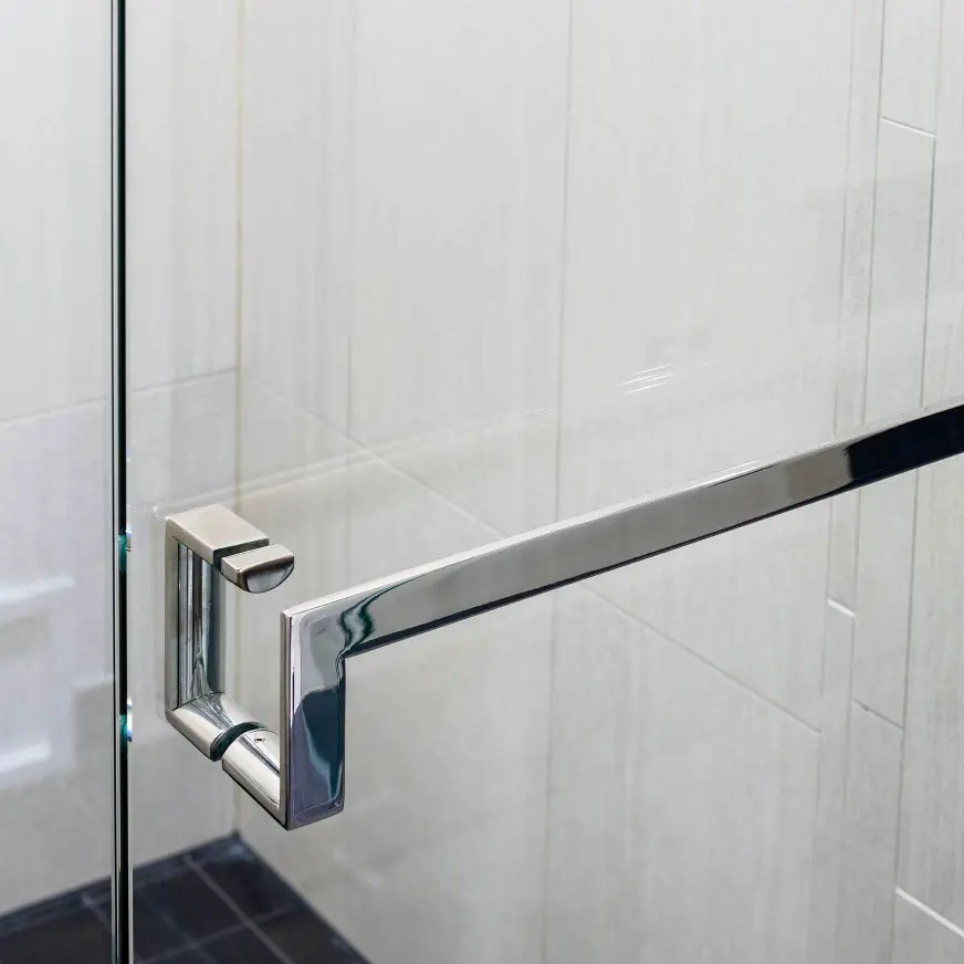 Polished chrome shower door pull handle with towel bar mounted on frameless glass enclosure