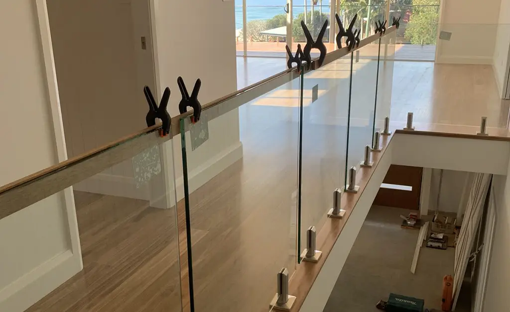 Frameless glass balustrade being installed with temporary clamps and stainless steel spigots on staircase