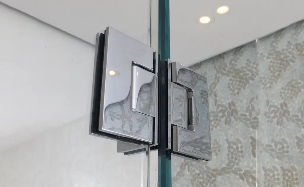 Chrome glass-to-glass hinge close-up showing installation detail on frameless shower enclosure