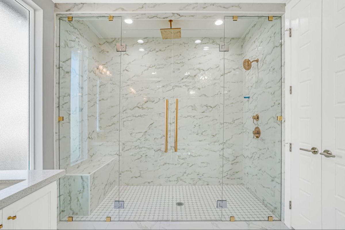 Luxury frameless shower enclosure with brass handles and glass clamps on marble tile walls