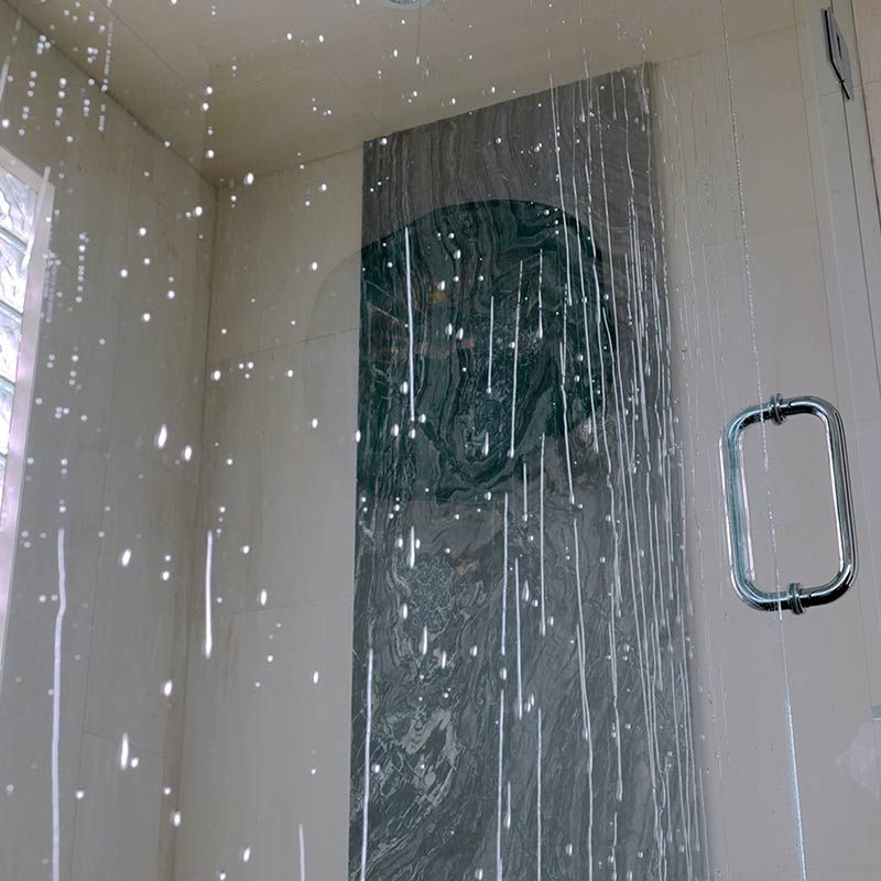 Water droplets on frameless shower glass door with chrome pull handle showing need for regular maintenance